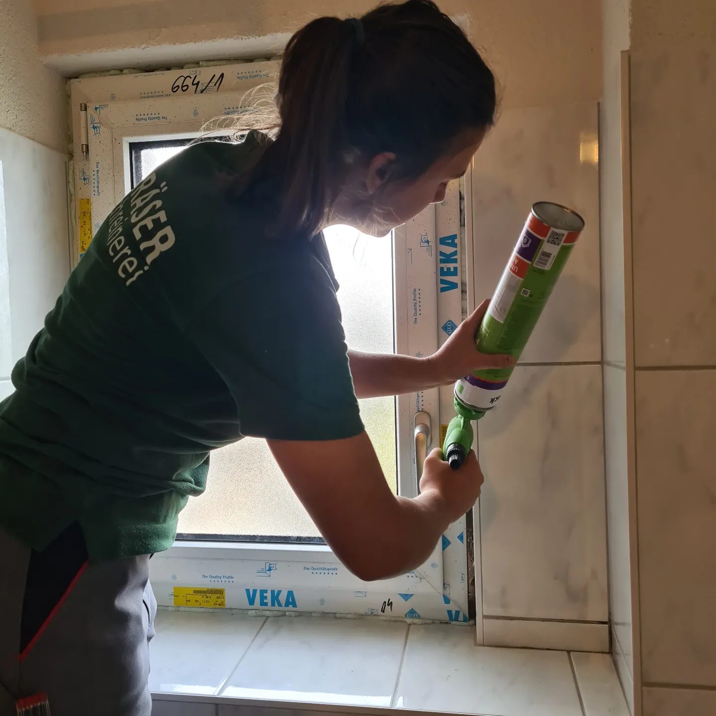 Mitarbeiterin im Gräser-Shirt beim Abdichten eines Fensters